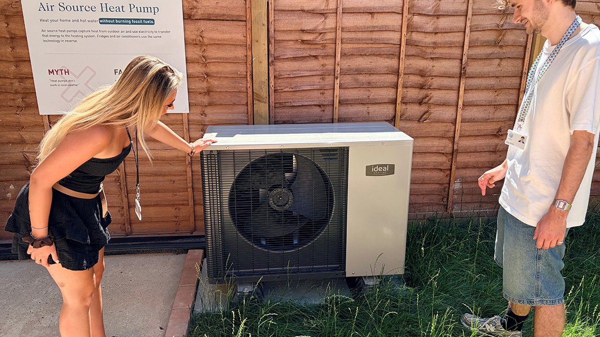Visitor leaning in to look at the air source heat pump in the garden while a staff member explains it
