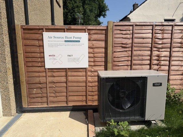 Air source heat pump in the garden with an information sign on the fence above