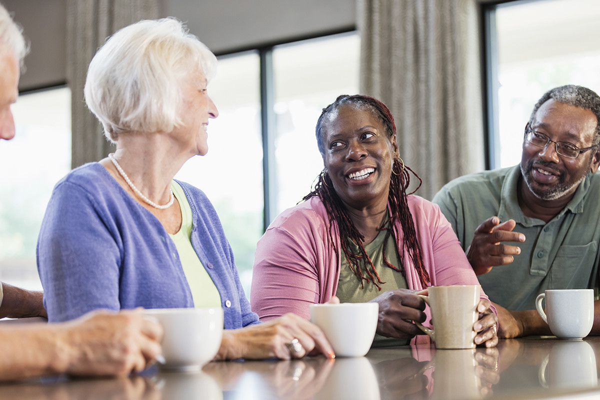 Older residents laughing and chatting over cups of tea at a table
