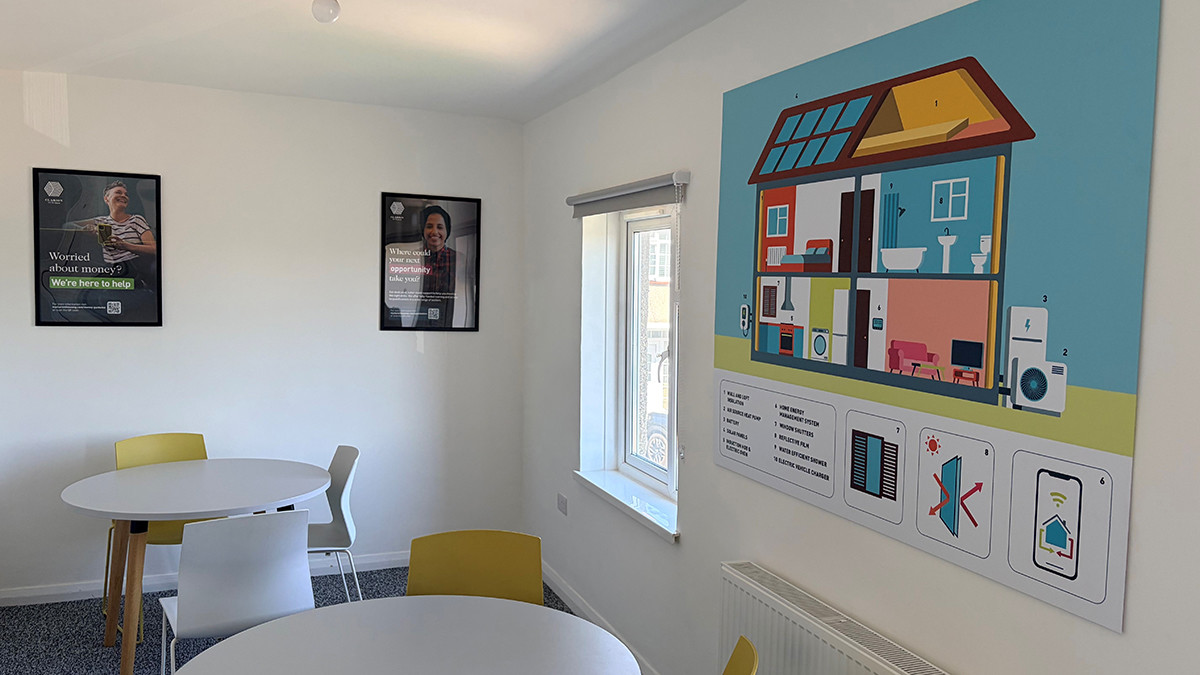Bright room inside the Green Community Home with tables, chairs and an illustrated poster of an energy-efficient house