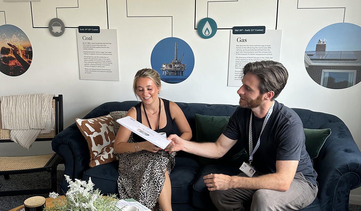 Clarion staff member handing a leaflet to a visitor on a sofa, with energy information posters on the wall behind